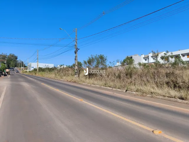Vista de uma estrada com vegetação seca e edifícios ao fundo.