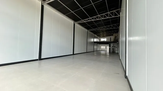 Corredor interno com paredes brancas e teto exposto.