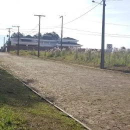 Vista externa de uma estrada de terra com postes de eletricidade em uma área rural.