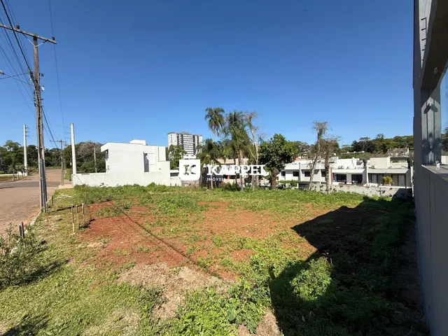 Vista externa de um terreno aberto com vegetação rasteira e construções ao fundo.