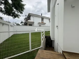 Vista da fachada de uma casa branca com muro e jardim.