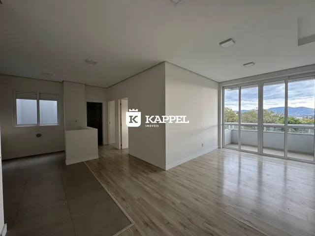 Vista de uma sala de estar com piso de madeira e acesso a uma varanda com vista para a paisagem.