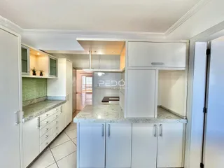 Vista interna de uma cozinha com armários brancos e bancadas de granito.