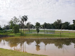 Paisagem de água e vegetação com campo ao fundo.