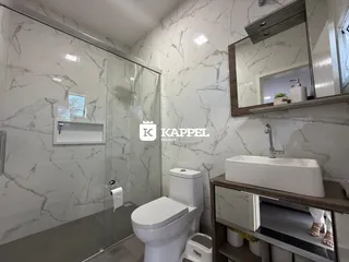 Banheiro com revestimento de mármore branco e box de vidro.