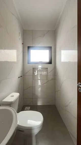 Corredor interno com revestimento de azulejos brancos e vasos sanitários.