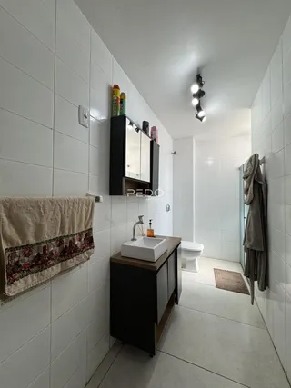 Hall de banheiro com revestimento branco e piso claro.