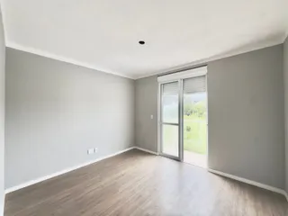 Sala de estar com piso de madeira clara e porta de vidro que dá para o jardim.
