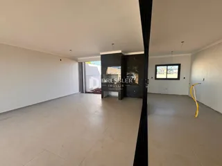 Interior de uma sala ampla com piso claro e paredes brancas.