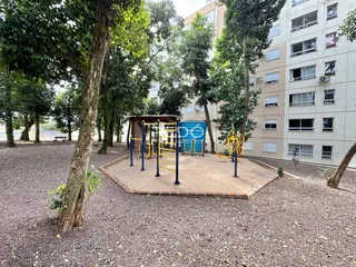 Área externa com playground e árvores em frente a um prédio residencial.