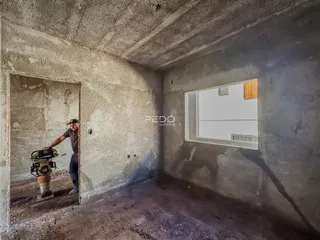 Interior de um cômodo com paredes de concreto aparente e uma porta de acesso.