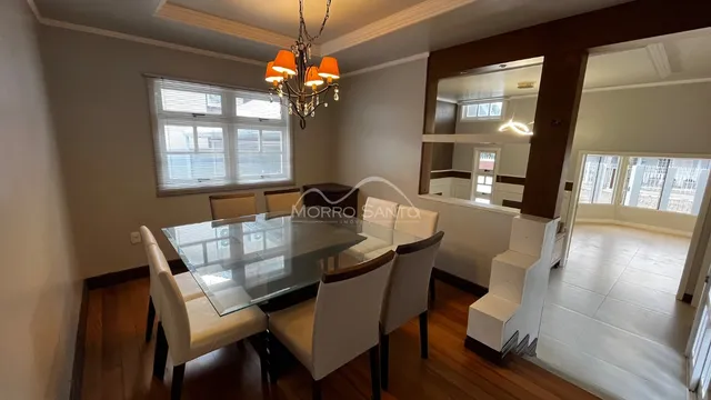 Sala de jantar com mesa de vidro e cadeiras brancas em um ambiente interno.