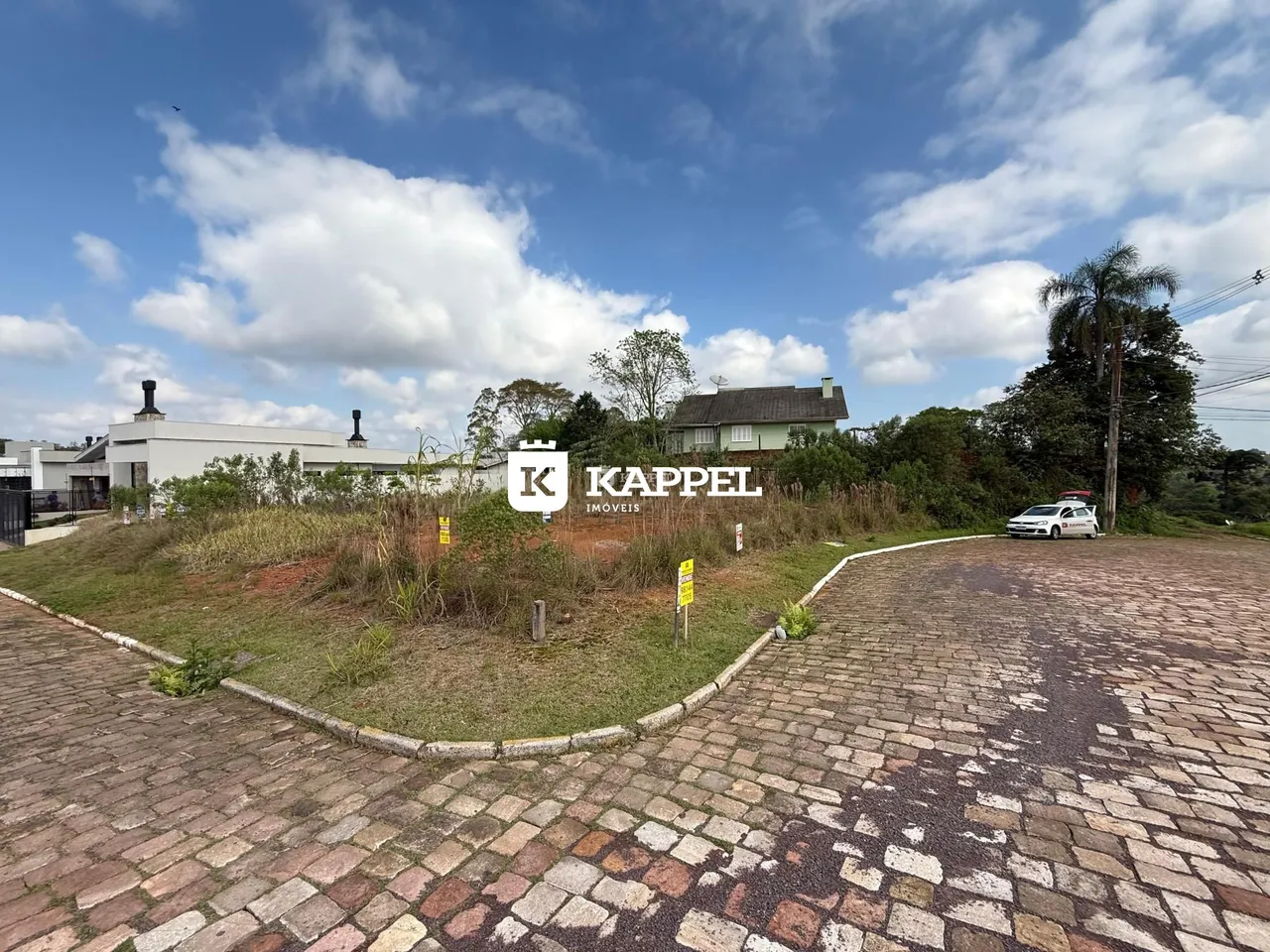 Vista externa de uma propriedade com paisagismo e uma estrada de paralelepípedos.