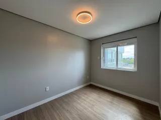 Ambiente interno com paredes cinzas e piso de madeira clara, mostrando uma janela com vista externa.