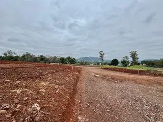 Uma estrada de terra vermelha atravessa uma área de campo aberto com vegetação ao fundo.