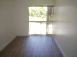 Vista interna de um cômodo com piso de madeira e grande janela.