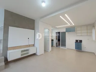 Sala de estar ampla com paredes brancas e piso claro.