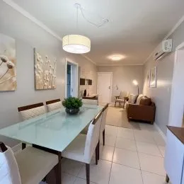 Sala de jantar com mesa de vidro e cadeiras brancas em um ambiente claro.