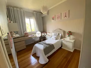 Quarto com cama de casal e janela com cortinas brancas.