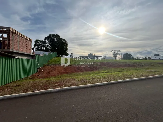 Vista externa de um terreno com cerca verde e vegetação ao lado de uma estrada.