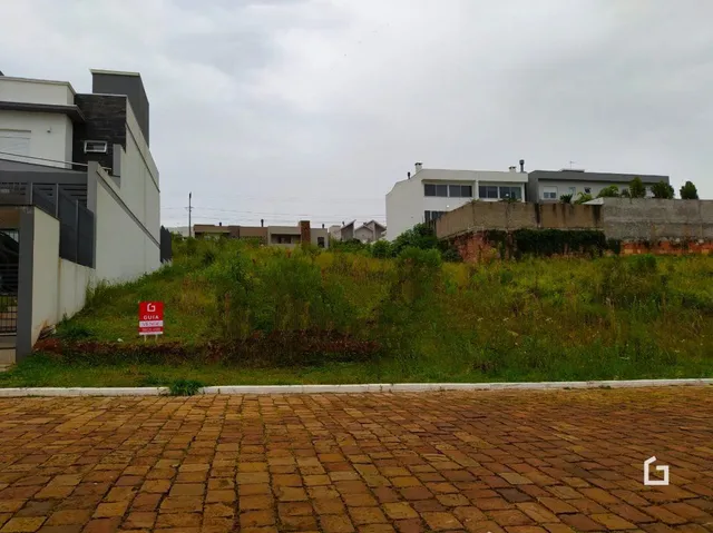 Vista externa da propriedade mostrando grama alta e um pátio de tijolos na frente da casa.