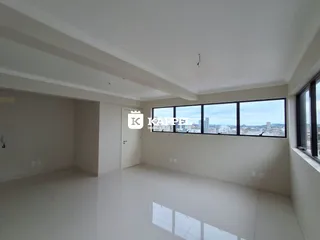 Sala ampla com piso claro e grande janela com vista da cidade.