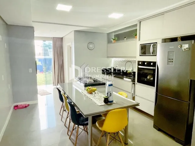 Ambiente interno de uma sala de estar com cozinha integrada e área de jantar.