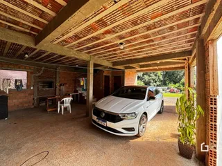 Interior de uma estrutura rústica com teto de telhas expostas e um carro estacionado.