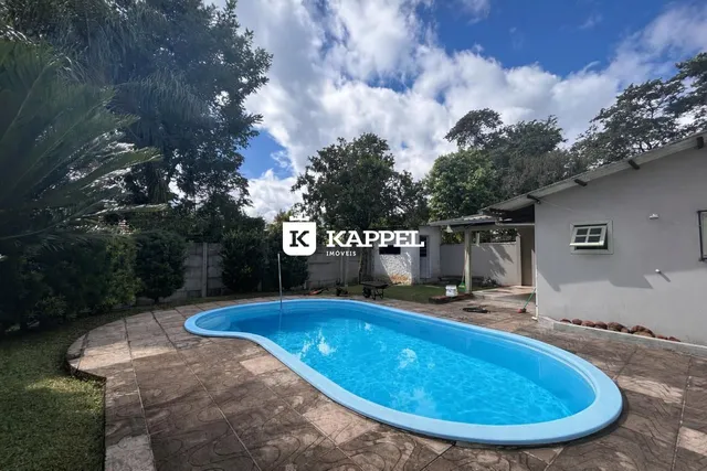 Piscina externa de formato curvo em um terreno com vegetação.