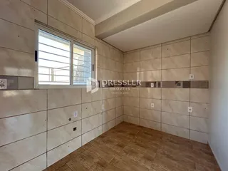 Interior de um cômodo com piso de madeira e paredes de azulejo claro.