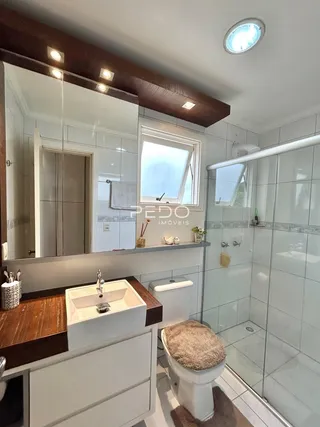 Foto do interior de um banheiro com box de vidro e azulejos brancos.