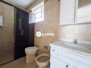 Banheiro com revestimento de azulejos claros e louças brancas.