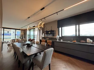 Sala de jantar com mesa de madeira e grandes janelas de uma residência.