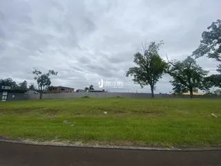 Vista externa de um terreno com gramado e árvores ao fundo.
