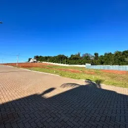 Vista externa do terreno com pavimento e vegetação sob um céu azul.
