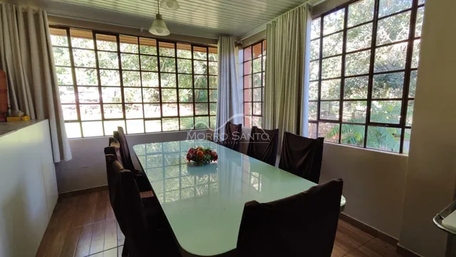 Uma sala de jantar com mesa de vidro e cadeiras escuras é vista em um ambiente bem iluminado.