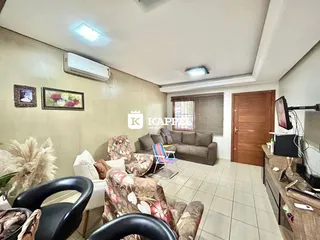 Sala de estar com sofá e poltronas em um ambiente claro com piso de cerâmica.