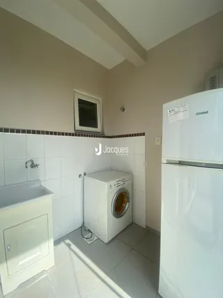 Interior de uma área de serviço com máquina de lavar e geladeira em um imóvel no Brasil.