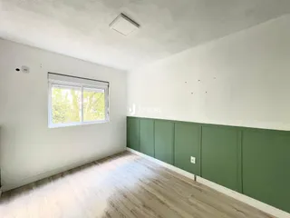 Ambiente interno de uma sala com paredes brancas e piso de madeira clara.