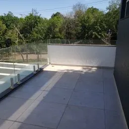 Vista de uma varanda com piso de concreto e grade de vidro.