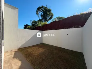 Vista lateral mostrando um muro branco e uma área gramada com um declive de terra ao fundo.