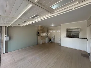 Interior de uma sala ampla com piso de cerâmica e teto com vigas expostas.