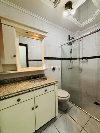 Foto de um banheiro com box de vidro e revestimento cerâmico.