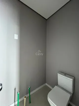 Um corredor interno com paredes cinzas e um vaso sanitário branco é visível na imagem.