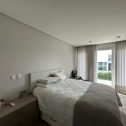 Quarto com cama de casal e cortinas brancas em um imóvel.