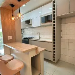 Uma cozinha com armários brancos e bancada clara é visível na foto.