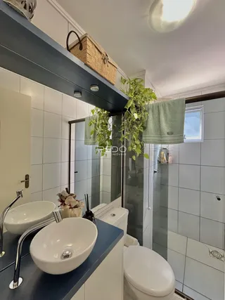 Banheiro com revestimento cerâmico branco e pias brancas.