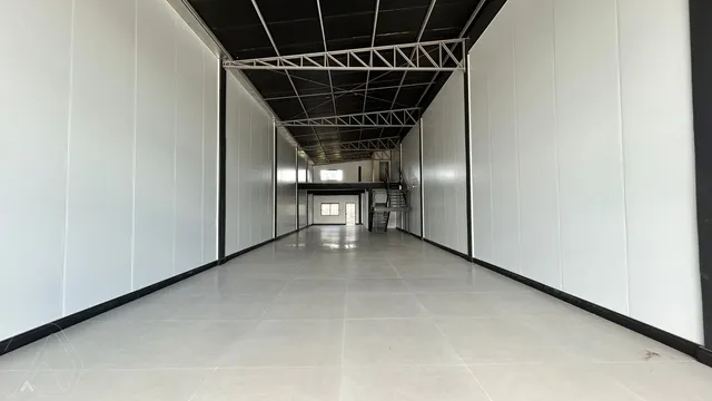 Corredor longo com paredes brancas e piso claro.