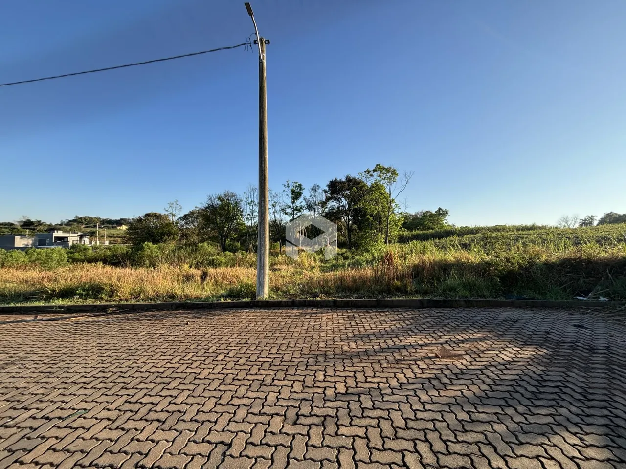 Vista externa de uma propriedade com grama seca e pavimento de tijolos.