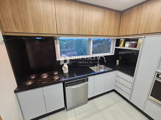 Vista da cozinha com armários de madeira clara e bancadas escuras.